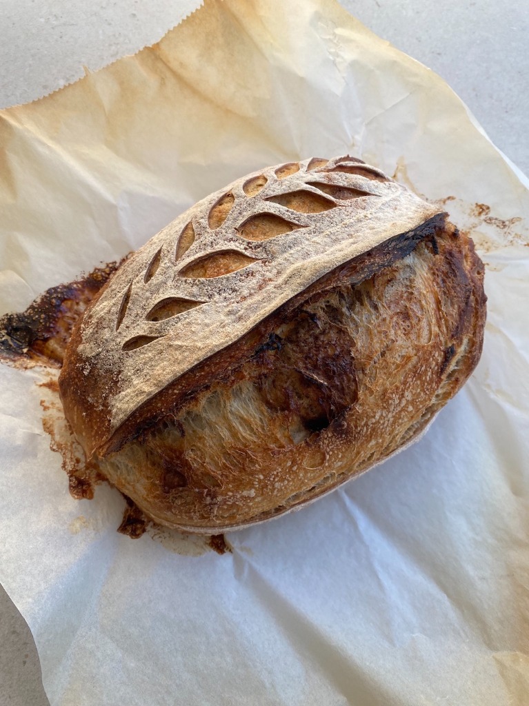Cinnamon brown sugar sourdough bread with caramelized crust and wheat pattern scoring on baking paper