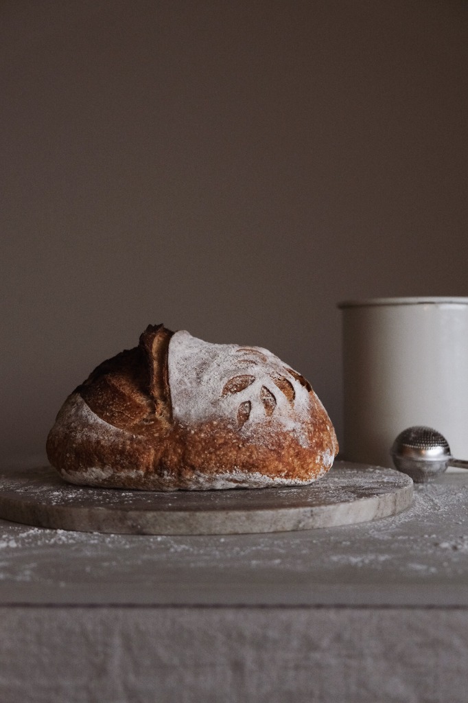 Freshly baked artisan sourdough loaf with a crisp golden-brown crust and wheat stalk scoring on a marble board