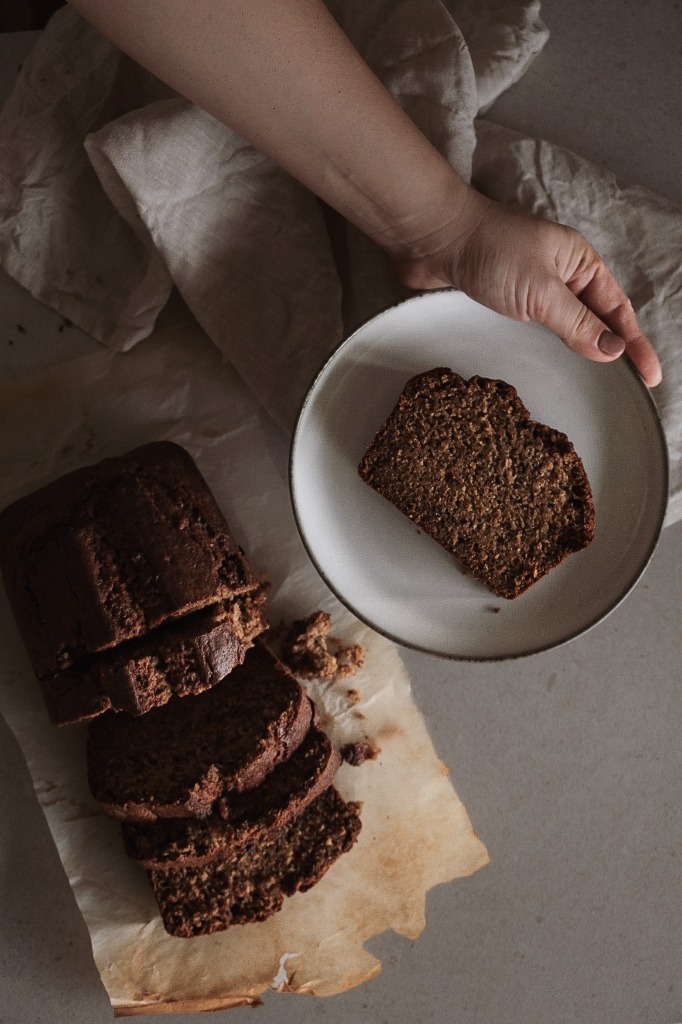 Sliced sourdough banana bread loaf alongside a plate with a generous tender slice served by hand